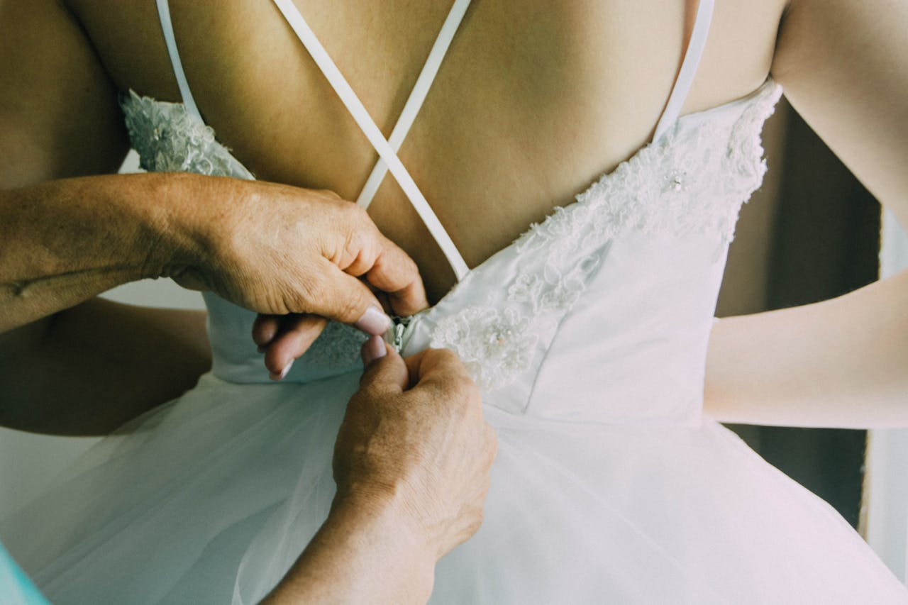 A close-up of a bride's dress being fastened, showcasing elegant lace details and wedding preparation.